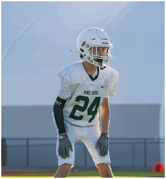 A person wearing a white football uniform with the number 24 and a helmet is standing on a field in a ready position. Description generated by AI