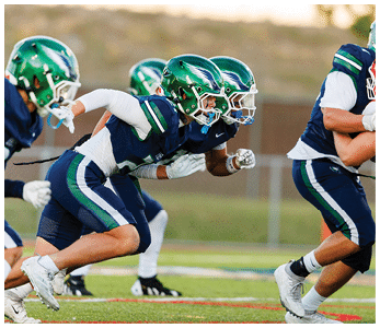 Several people in green helmets and blue sports uniforms are running on a football field during a game or practice. Description generated by AI