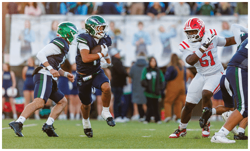 Three people in football uniforms are actively engaged in a play on a grassy field with a crowd in the background. Description generated by AI