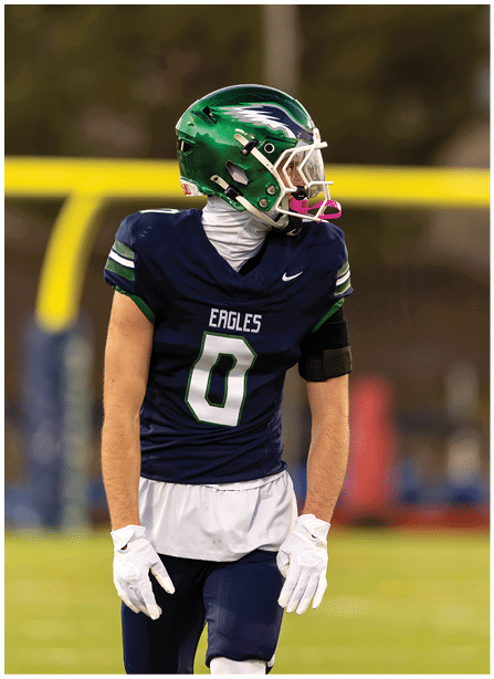 A person wearing a green helmet and navy blue football uniform with the word Eagles and the number 0 stands on a football field looking to the side. Description generated by AI