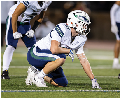 A person wearing a white and blue football uniform with the number 25 is kicking a football on a field at night. Description generated by AI