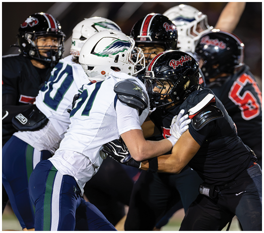 Two football players in black uniforms with “Raptors" on their pants are engaged in a play with one preparing to throw the ball while a player in a white and blue uniform attempts to block or tackle. Description generated by AI