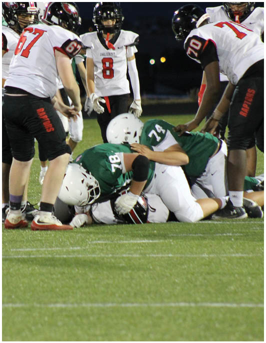 Several people wearing football uniforms are on a field at night, with one person on the ground and others standing nearby. Description generated by AI