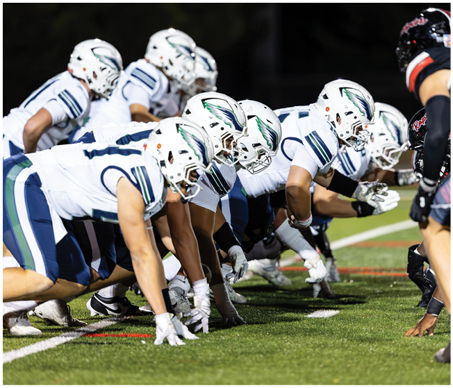 Two opposing American football teams are lined up facing each other on a field, ready for the next play. Description generated by AI