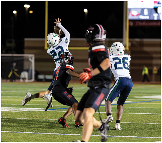 Two people in white and blue sports uniforms are playing football against two people in black and red uniforms on a lit field at night. Description generated by AI