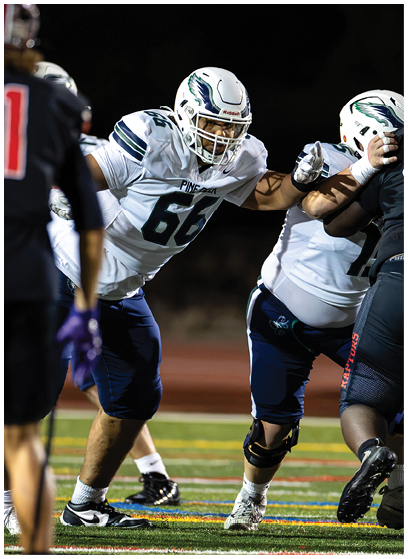 People wearing football uniforms are engaged in a play on a lit field during a game at night. Description generated by AI
