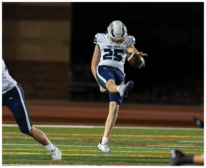 A person wearing a white and blue football uniform with the number 25 is kicking a football on a field at night. Description generated by AI