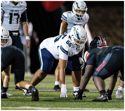 People in football uniforms are positioned on a field preparing for a play during a game. Description generated by AI