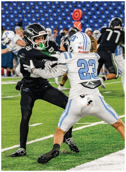 Two football players in helmets and uniforms are engaged in a physical play on a green field during a game. Description generated by AI