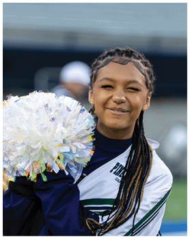 A person wearing a cheerleading uniform is smiling and holding a large white pom-pom. Description generated by AI