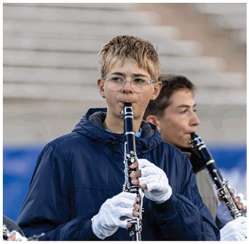 Two people wearing jackets and white gloves are playing clarinets outdoors with blurred steps in the background. Description generated by AI
