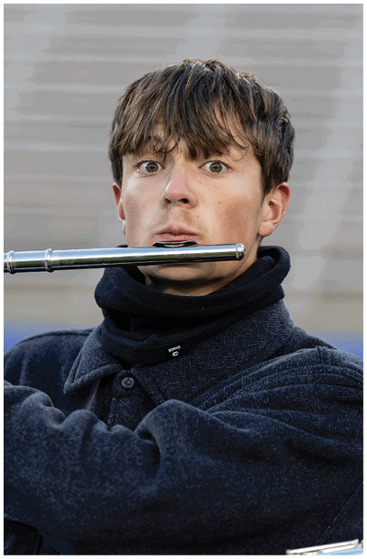 A person wearing white gloves and a dark jacket is playing a silver flute against a blurred background. Description generated by AI
