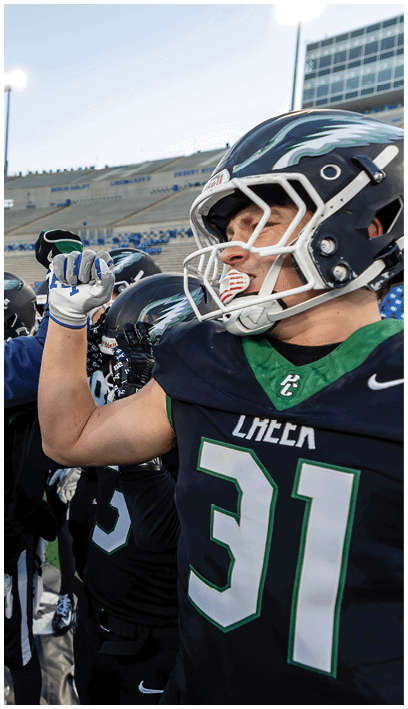 A group of people wearing football helmets and uniforms are on the sidelines of a stadium, with one person raising a fist in a gesture of encouragement or celebration. Description generated by AI