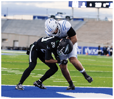 Two football players in action on the field with one player in a white uniform tackling another player in a black uniform. Description generated by AI