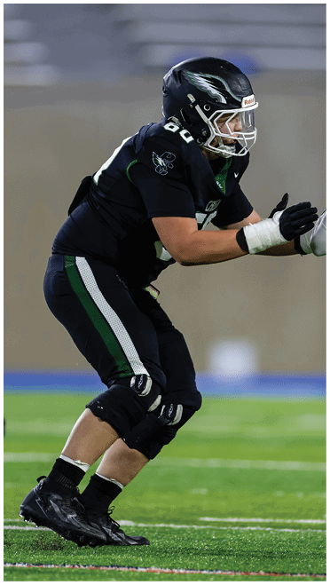 Two people in football uniforms are engaged in a play on a green field with one person in black reaching toward the person in white. Description generated by AI