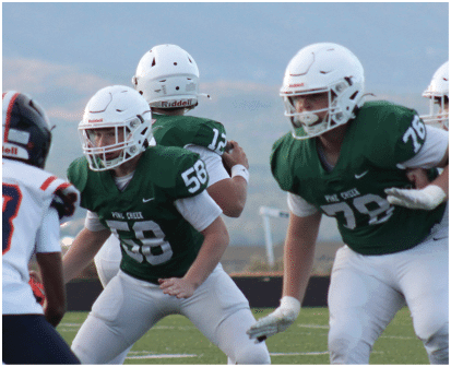 People wearing football helmets and green jerseys are engaged in a game or practice on an outdoor field. Description generated by AI