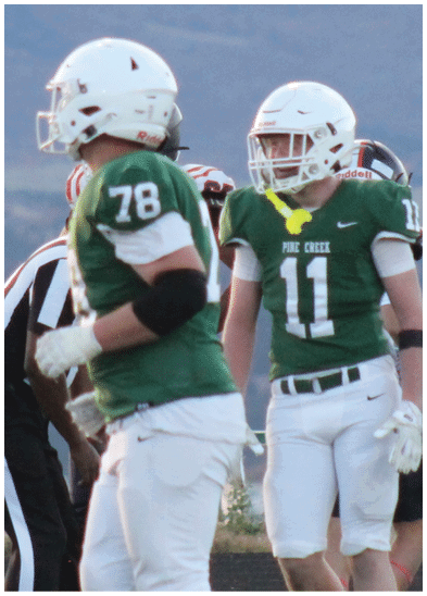 A person wearing a green football jersey with the number 78 and white pants is standing on a field with other players in the background. Description generated by AI