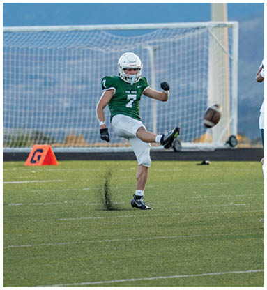 Four people in football uniforms are on a field with one person kicking a football while the others are running nearby. Description generated by AI
