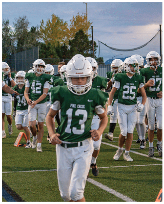 A group of people wearing green and white football uniforms and helmets are walking on a football field during what appears to be a practice or warm-up session. Description generated by AI