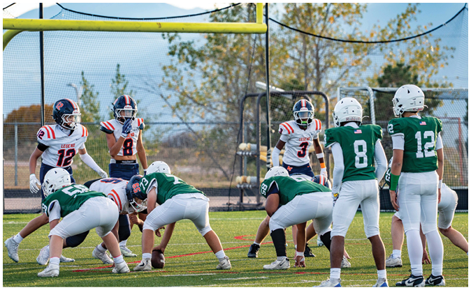People in football uniforms are positioned on a field under a goalpost, preparing for a play during a game. Description generated by AI