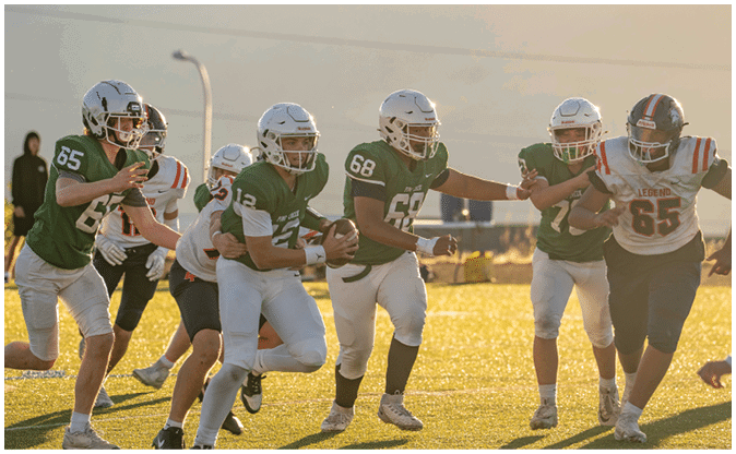 A group of people wearing football helmets and uniforms are actively engaged in a game on a sunlit field. Description generated by AI