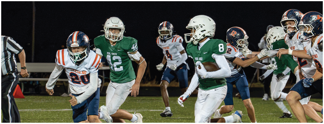 Children in football uniforms are actively running and playing on a grassy field during a nighttime game. Description generated by AI