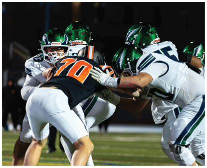 Several people wearing football helmets and uniforms are engaged in a close physical play on a football field. Description generated by AI