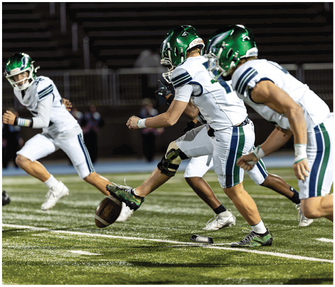 People in football uniforms with green helmets are actively kicking and running on a grassy field during a game. Description generated by AI