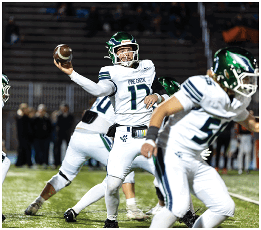 A person wearing a white football uniform with “Pine Creek" on the chest is preparing to throw a football during a nighttime game. Description generated by AI