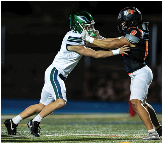 Two football players in full gear are engaged in a physical contest on the field during a nighttime game. Description generated by AI