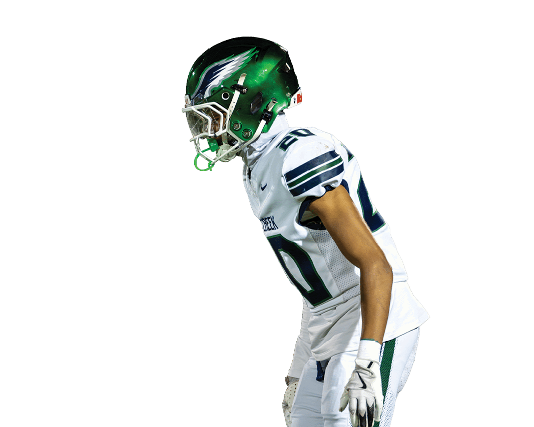 A person wearing a green football helmet and white uniform is leaning forward in a ready stance. Description generated by AI