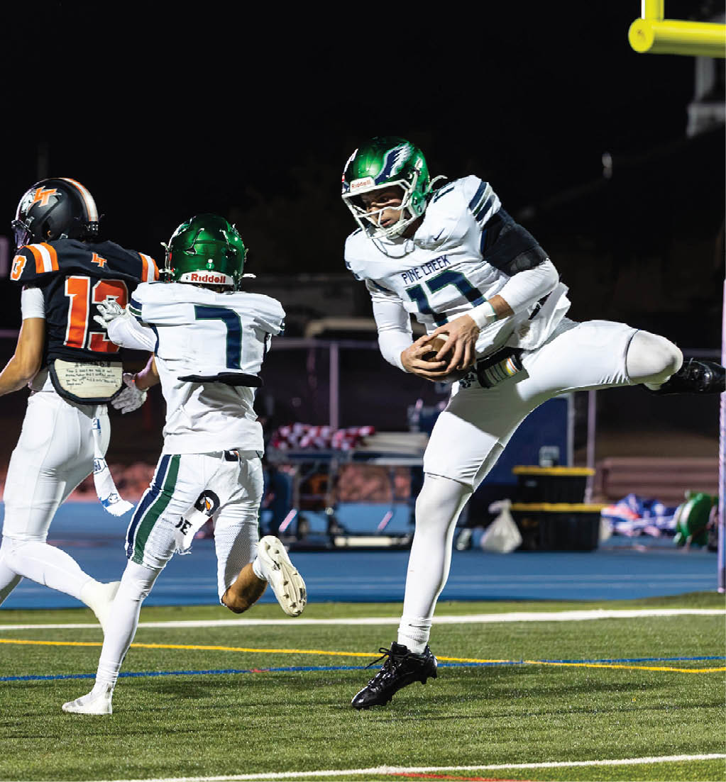 Three people in football uniforms are actively playing on a field at night, with one person in white and green leaping while holding the ball. Description generated by AI