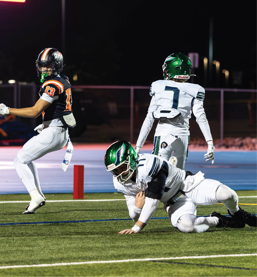 Three football players in uniforms and helmets are on a field at night with one player running, one standing, and one falling to the ground. Description generated by AI