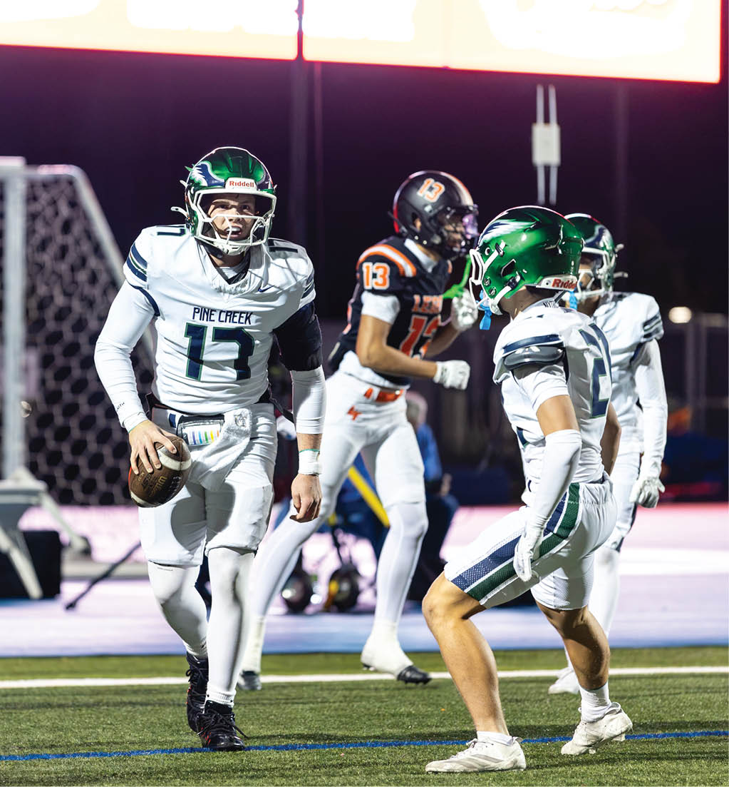 Three people in football uniforms are on a field at night, with one person holding a football and others appearing to prepare for a play. Description generated by AI