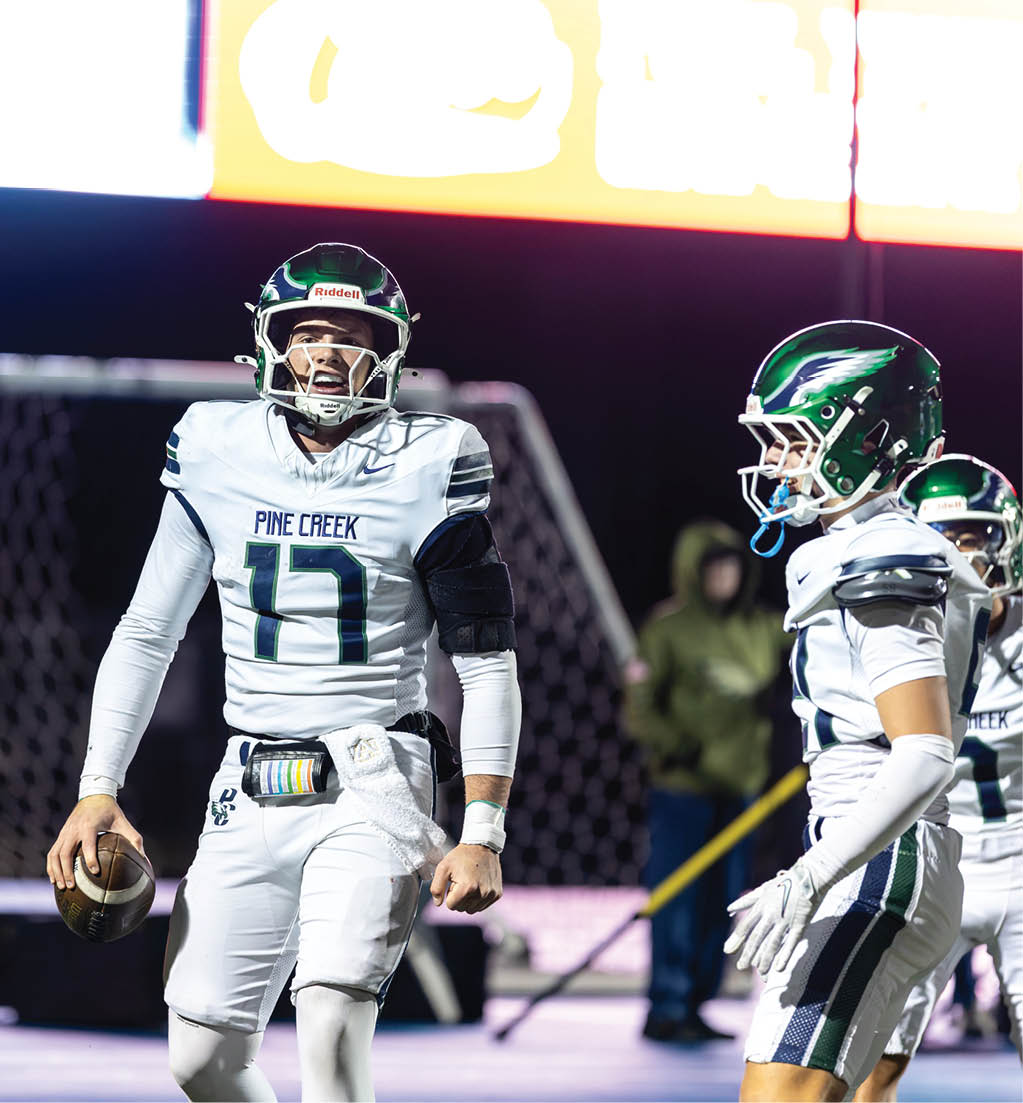 Two people in white football uniforms with green helmets are on a field, with one holding a football and appearing to prepare for a play. Description generated by AI