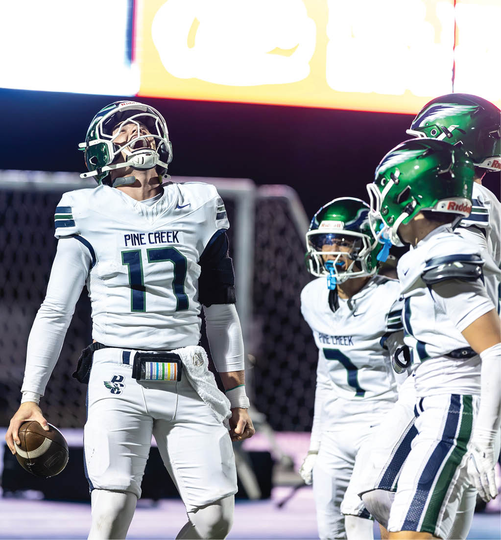 A group of football players in white uniforms with green helmets are celebrating on the field, with one player holding a football and looking upward. Description generated by AI