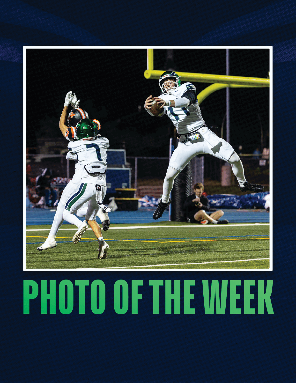 Two people in football uniforms are actively reaching for a football near the goalpost on a field at night with one person jumping in the air and the other preparing to catch the ball. Description generated by AI