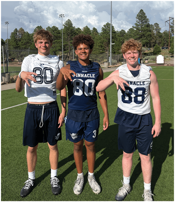 Three football players in blue and white uniforms running on a field. Description generated by AI