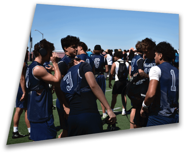 Four people in dark football uniforms and helmets stand in a row on a field, appearing focused and ready for action. Description generated by AI