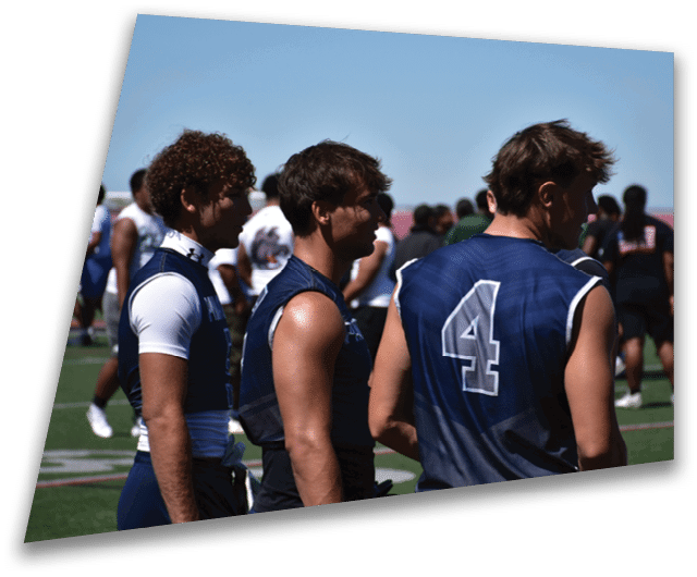 Four people in dark football uniforms and helmets stand in a row on a field, appearing focused and ready for action. Description generated by AI
