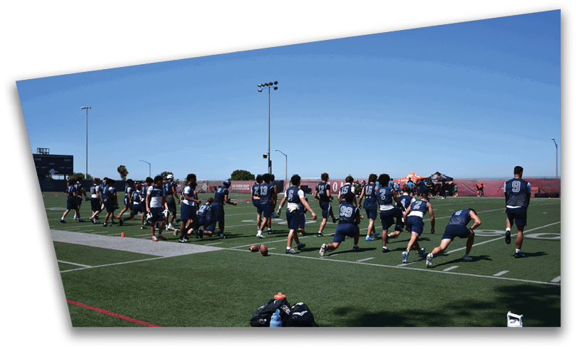 People wearing black American Canyon football uniforms and helmets are standing on a football field at night. Description generated by AI