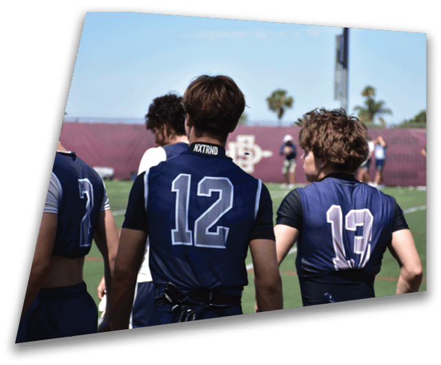 Four people in dark football uniforms and helmets stand in a row on a field, appearing focused and ready for action. Description generated by AI