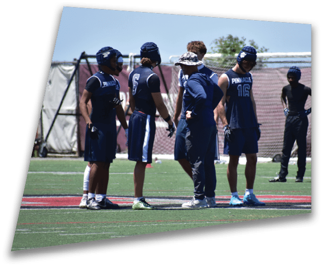 Four people in dark football uniforms and helmets stand in a row on a field, appearing focused and ready for action. Description generated by AI
