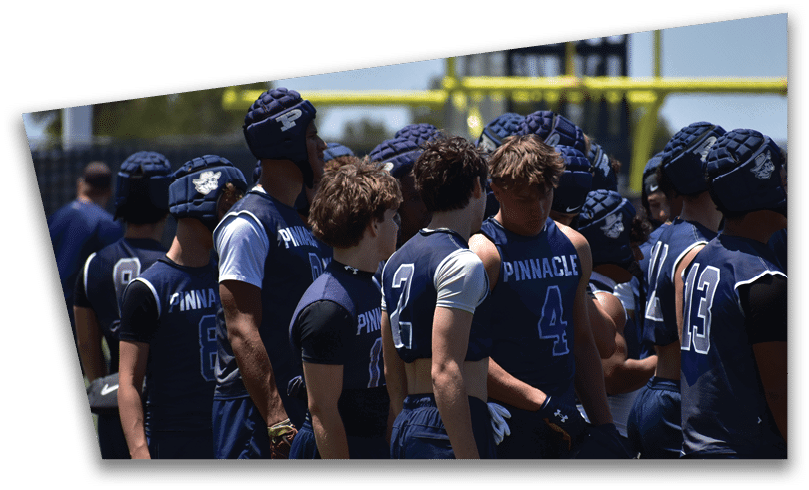 People wearing black American Canyon football uniforms and helmets are standing on a football field at night. Description generated by AI