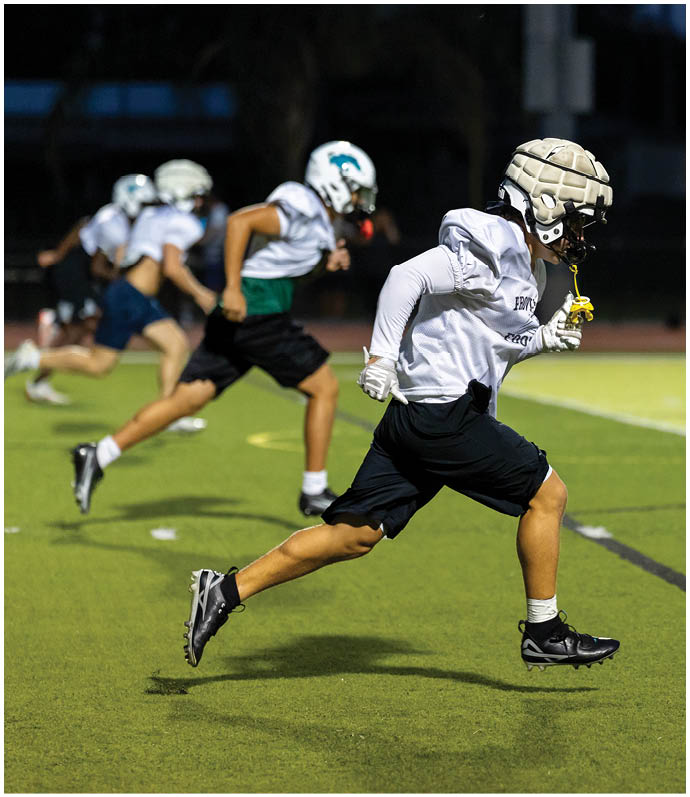 Three football players in blue and white uniforms running on a field. Description generated by AI