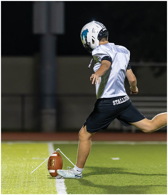 Three football players in blue and white uniforms running on a field. Description generated by AI