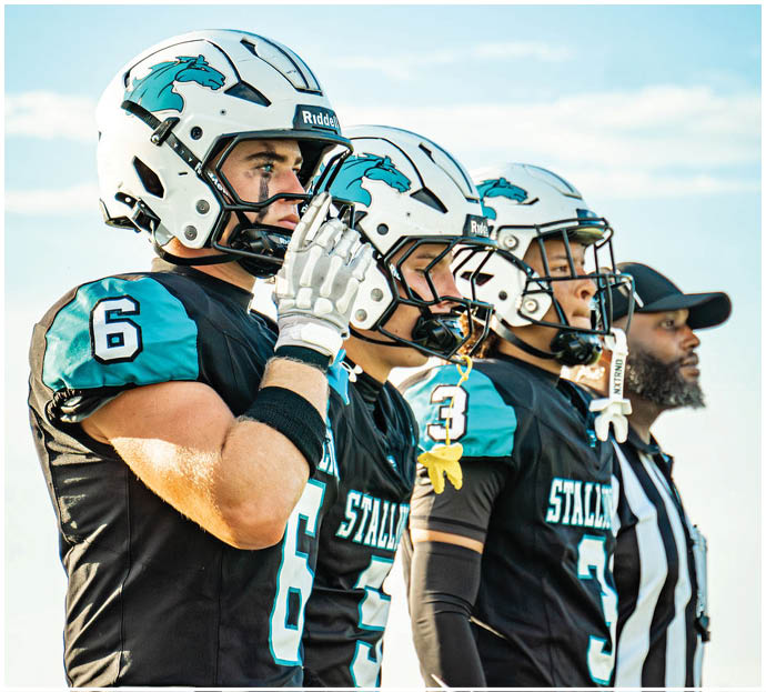 Three football players in blue and white uniforms running on a field. Description generated by AI