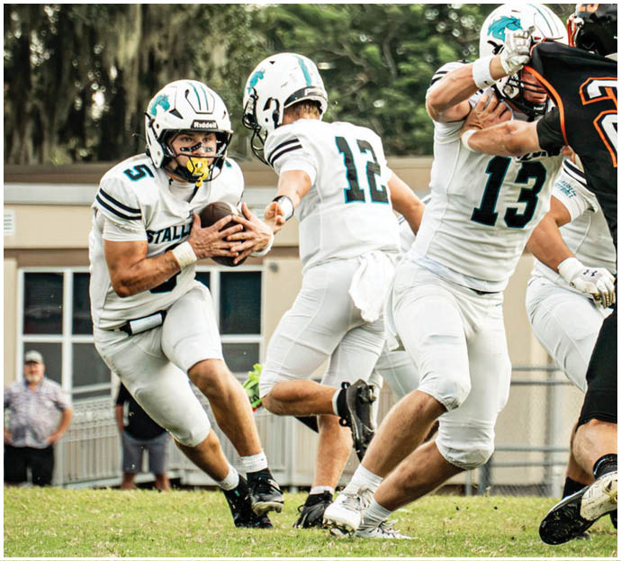 Three football players in blue and white uniforms running on a field. Description generated by AI