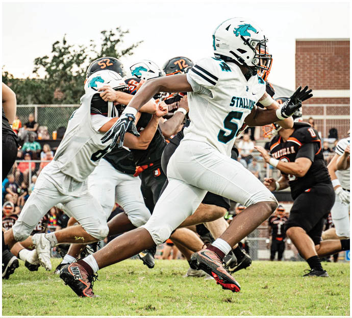 Three football players in blue and white uniforms running on a field. Description generated by AI