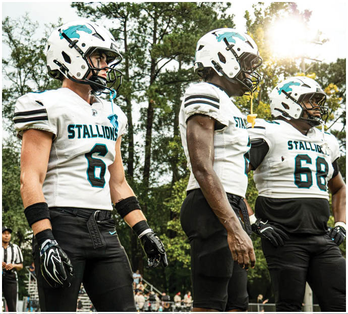 Three football players in blue and white uniforms running on a field. Description generated by AI